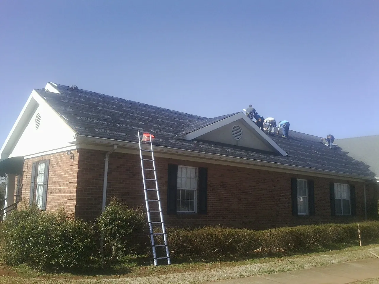 Crew tearing shingles off a brick ranch roof with a ladder set — Emergency Roof Repair work by our crew in Duffield