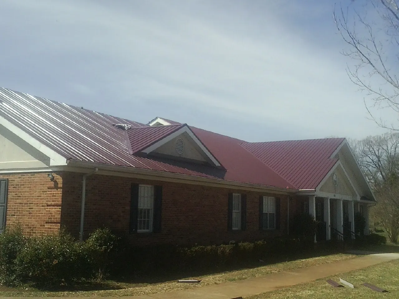 Red metal roof with gabled entries on a long brick building, from a Hail Damage Roof Repair job in Duffield