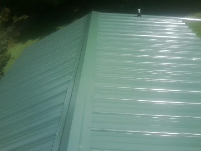 New green metal panels meeting at the ridge of a roof — Flat Roof Repair work by our crew in Duffield