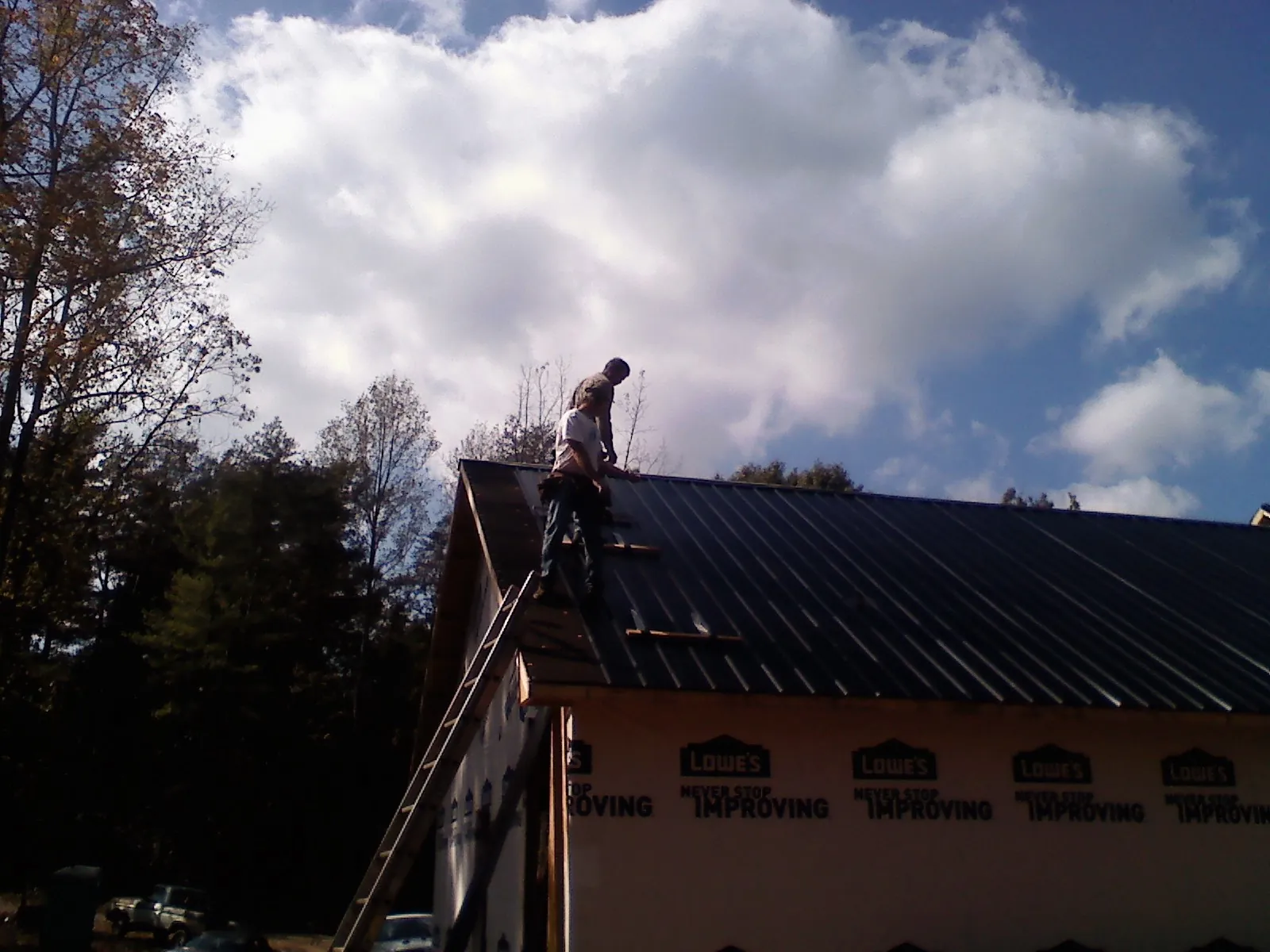 Roofer fastening dark metal panels high against a cloudy sky, from a Roof Inspection job in Duffield