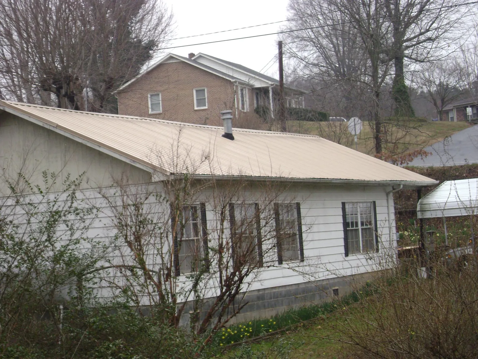 Tan metal roof on a white sided house set into a hillside — Commercial Roofing by Roofing Brothers in Duffield