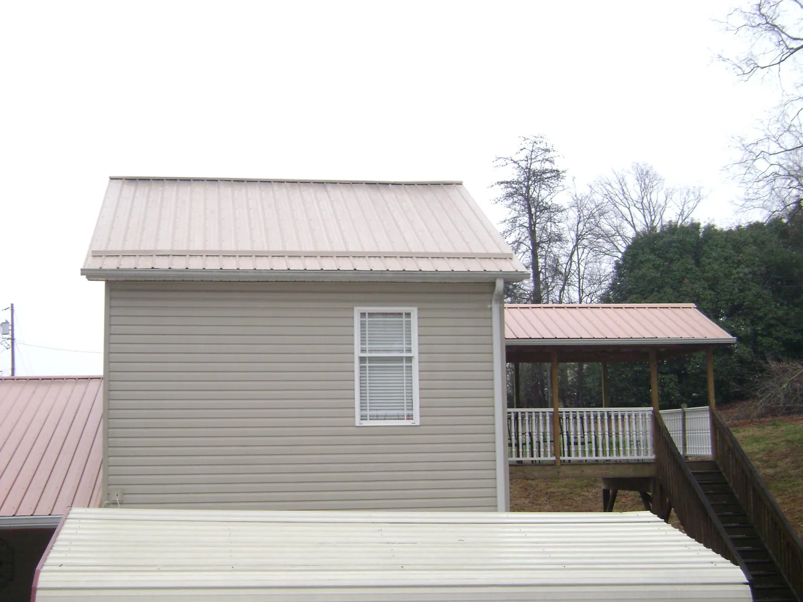 Tan metal roofs on a two story addition and attached porch, from a Roof Replacement job in Duffield